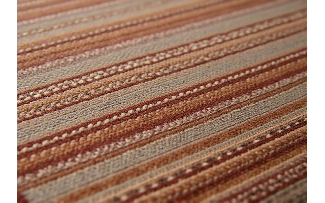 Gros plan sur un tapis tissé à la main, montrant la richesse des textures et les motifs géométriques subtils dans des tons terreux.